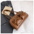 Detailed view of brown patent leather bag with front bow pockets on a white bed sheet - Brown