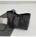 Detalle de un bolso tote gris oscuro con placa de logotipo plateada y remaches metálicos - Negro