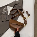 Braune halbrunde Satteltasche aus mattem Leder mit zwei Riemen auf weißem Bett - Braun