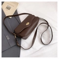 Detail of dark brown leather crossbody bag with a gold twist lock on a white fabric backdrop - Coffee