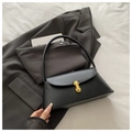 Detalle del bolso de cuero negro con hebilla dorada sobre una chaqueta americana gris - Negro