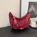 Close-up of burgundy nylon crescent bag with wide strap and braided zipper detail - Red