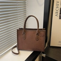 Brown embossed clover tote bag with top handles and adjustable strap in lifestyle setting - Brown