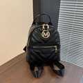 Mini zaino in pelle trapuntata nera con logo M dorato su un tavolo in legno scuro - Nero