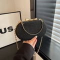 Detail view of a black evening clutch bag with glitter finish and golden bow clasp - Black