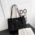 Detail of black quilted tote bag with brown straps against a minimalist backdrop - Black