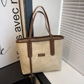 Detail of canvas tote bag with brown leather handles and brand patch on display shelf - Beige