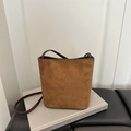 Détail d'un sac seau en daim marron avec bandoulière posé sur un livre vintage - Fauve