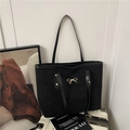 Elegante bolso tote de ante negro con lazo dorado para mujer sobre maleta blanca - Negro