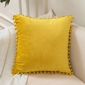 Bright yellow velvet cushion cover with pom-pom fringe edges on a home sofa - Yellow