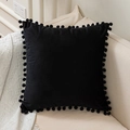 Solid black velvet pillow cover with pom-pom fringe edges on a modern beige sofa - Black