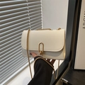 Close-up of minimalist cream crossbody bag featuring a golden oval metal lock and chain strap - White