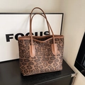 Close-up of leopard print tote bag with brown leather handles on wooden surface - Brown