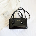Detailansicht einer glänzenden schwarzen Lackledertasche mit goldenem Mode-Schriftzug - Schwarz