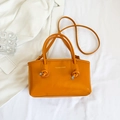 Detail der glänzenden orangefarbenen Handtasche mit Knotengriffen und Schriftzug - Orange