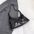 Glossy black hobo shoulder bag with gold zipper detail on grey blazer suit background - Black