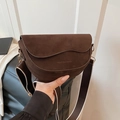 Detail of dark brown suede saddle bag featuring wave-edged flap and wide fabric strap - Brown