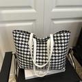 Detail view of large houndstooth tote bag with white leather straps on black chair - Black