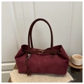 Detail of burgundy suede tote with leather handles and metallic buckle on a cozy setup - Red