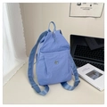 Close-up of light blue nylon backpack showing fine texture and a circular metal M logo - Blue
