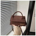 Makroansicht der braunen Wildleder-Umhängetasche mit Goldlogo und Lichtschatten - Kaffeebraun