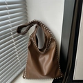 Braune Hobo-Tasche aus Leder mit silbernen Nieten an einer weißen Wand mit Schattenwurf - Braun