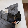 Bolso de hombro en charol negro brillante con hebilla plateada sobre fondo de traje gris - Negro