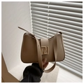 Detalle de bolso baguette en cuero beige con hebilla dorada frente a una pared blanca - Caqui