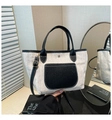 Detail of woven straw tote bag featuring black leather handles and metallic snap closure - Black