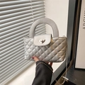 Silberne Stepptasche mit Herzschloss und Kettenriemen für Damen in der Hand getragen - Silber