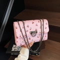 Pink crossbody bag with red cherry prints and silver chain strap on a wooden background - Pink
