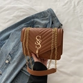 Detail of brown quilted chain bag with gold logo and tassel on denim backdrop - Brown