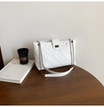 Close-up of white quilted crossbody bag featuring a silver metal turn-lock on a wooden table - White