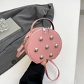 Roze ronde crossbodytas met zilveren studs en handvat, lifestyle-weergave in de hand - Roze