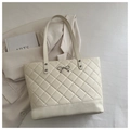 Detail of cream quilted tote bag featuring silver bow charm and elegant stitching - White