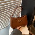 Borsa sottospalla marrone coccodrillo con fiocco dorato appoggiata su un libro - Marrone