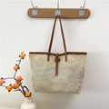 Grande borsa tote in paglia con manici in pelle marrone appesa a una parete bianca - Marrone