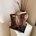 Chic brown lychee grain leather tote bag displayed on books with artistic decor - Brown