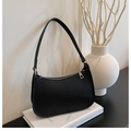 Close-up of black lychee grain leather underarm bag with silver zipper on white books - Black