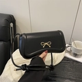Elegant black crossbody bag with golden bow closure shown in a lifestyle setting - Black
