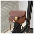 Close-up of caramel leather saddle bag featuring a large rectangular gold metal lock detail - Brown