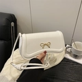 Elegant white shoulder bag with golden bow hardware on a classic wooden tabletop - White