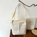 Minimalist beige pleated bucket bag with decorative lace bow charm on a wooden table - Off White