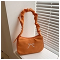 Detail of orange ruched handle bag with white bow embroidery on a minimalist setup - Orange