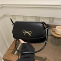 Women's black leather crossbody bag featuring a golden bow buckle and elegant curved shape - Black