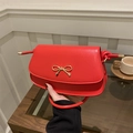 Elegant red shoulder bag with gold bow clasp and sleek leather finish in a lifestyle setting - Red