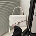 White faux leather crossbody bag with golden oval buckle and top handle shown on a table - White