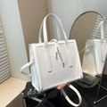 Elegante weiße quadratische Handtasche mit Goldakzenten und langem Schultergurt im Fokus - Weiß