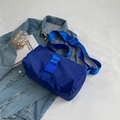 Royal blue nylon cylindrical crossbody bag with wide shoulder strap on denim background - Klein Blue
