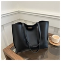 Detail of minimalist black leather tote bag with metal buckle on a wooden table - Black